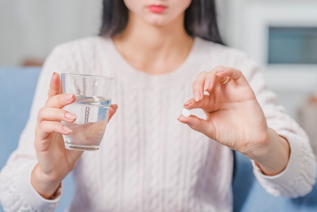 Mittlerer Abschnitt einer Frau, die weiße Tablette und Glas Wasser in den Händen hält