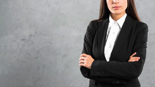 Mittlerer Abschnitt einer Geschäftsfrau, die mit dem Arm steht, kreuzte gegen grauen Hintergrund