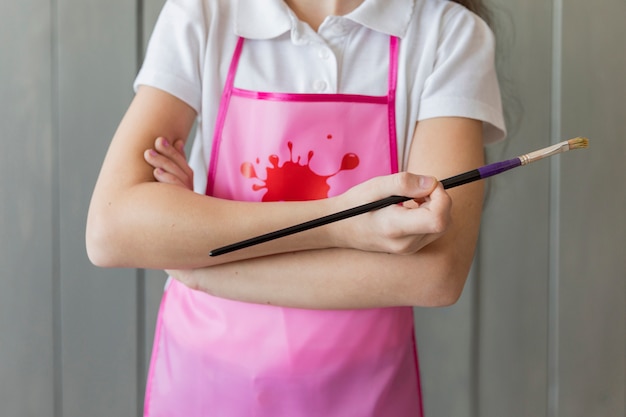Mittlerer Abschnitt einer Mädchenholdingstellung mit dem Arm kreuzte in der Hand, Malerpinsel halten