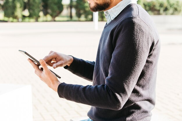 Mittlerer Abschnitt eines Mannes, der im Park unter Verwendung des Touch Screen Handys sitzt