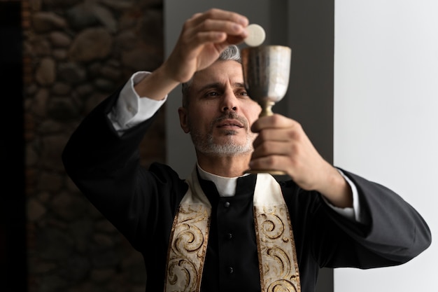 Kostenloses Foto mittlerer aufnahmepriester, der eucharistie hält