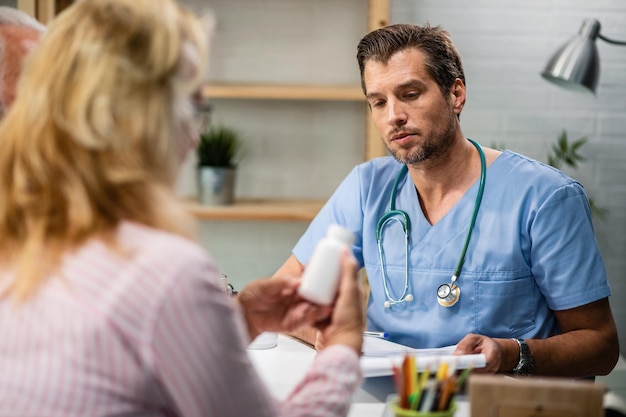 Mittlerer erwachsener Arzt, der während der Konsultationen mit seinen Patienten über die medizinische Pillenbehandlung spricht