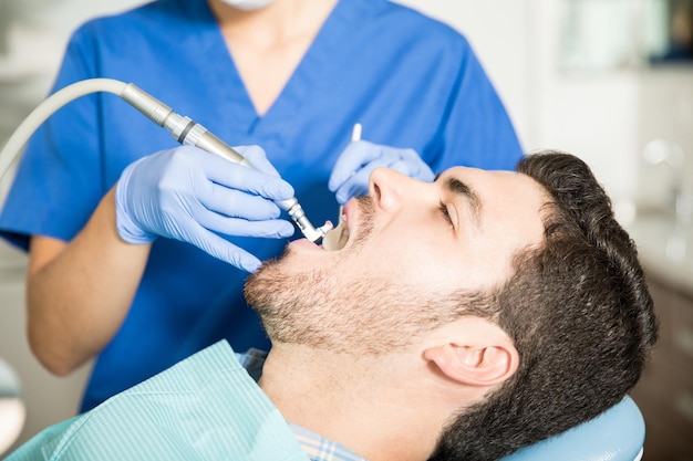 Mittlerer erwachsener Mann, der in der Klinik eine zahnärztliche Behandlung von einer Zahnärztin erhält
