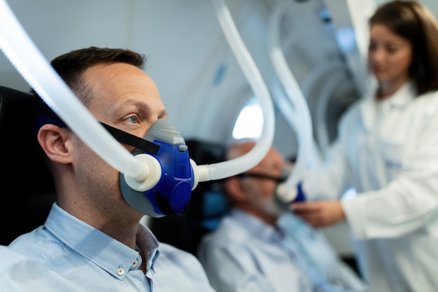Mittlerer erwachsener Mann, der während der hyperbaren Sauerstofftherapie in der Klinik durch Maske atmet