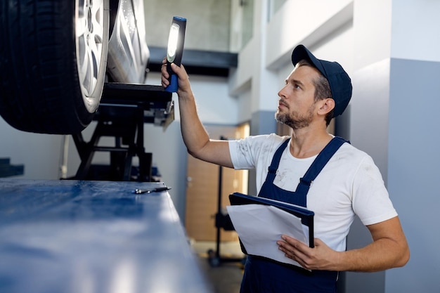 Mittlerer erwachsener Mechaniker, der Taschenlampe benutzt, während er Auto in der Autowerkstatt untersucht