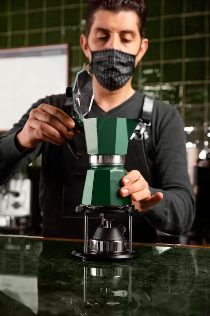 Mittlerer Schuss Barista mit Maske, die Kaffee vorbereitet