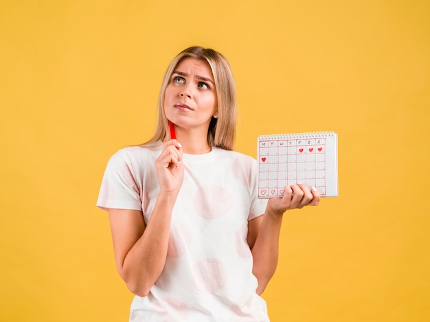 Mittlerer Schuss der Frau den Zeitraumkalender denkend und halten