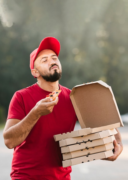 Kostenloses Foto mittlerer schuss erfüllter lieferbote, der pizza isst