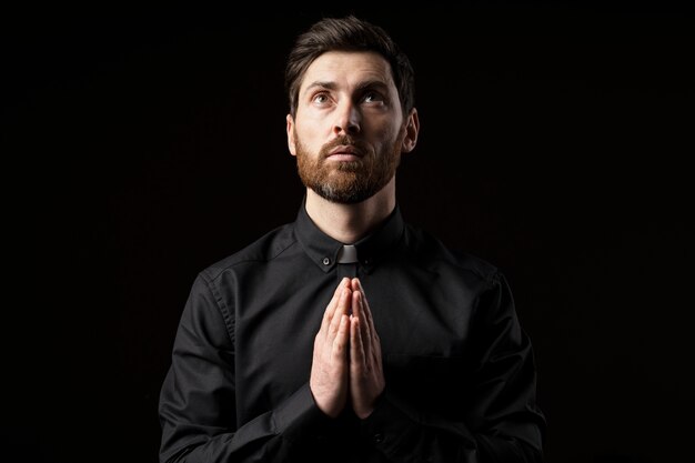 Mittlerer Schuss junger Priester, der mit dunklem Hintergrund betet