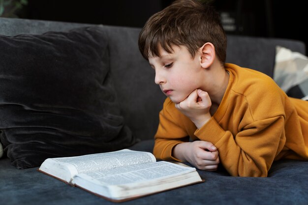 Mittlerer Schuss kleiner Junge liest Bibel auf der Couch