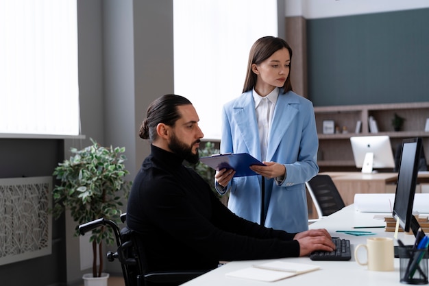 Mittlerer Schuss Mann im Rollstuhl, der im Büro arbeitet