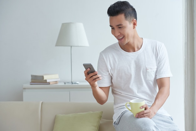 Mittlerer Schuss von beschäftigtem SMS des jungen Darms in seinem Social Media auf Smartphone morgens