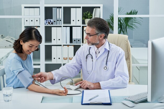 Mittlerer Schuss von Doktor Blutdruck des weiblichen Patienten überprüfend