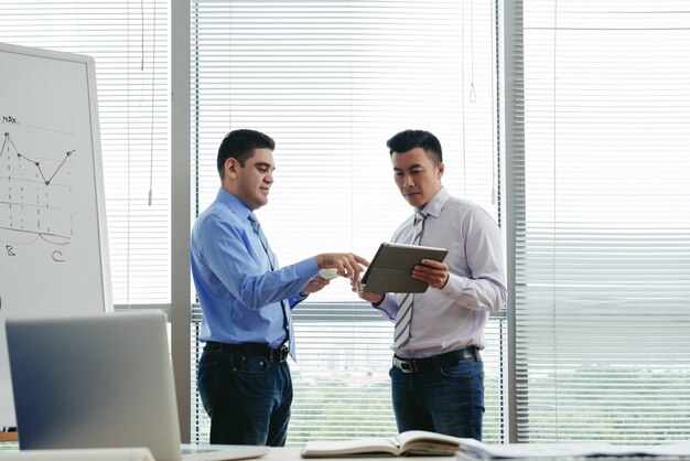 Mittlerer Schuss von zwei Kollegen, die im Büro stehen und Daten bezüglich des Tablet-PCs besprechen