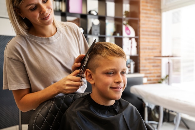 Kostenloses Foto mittlerer schussjunge, der im salon die frisur bekommt