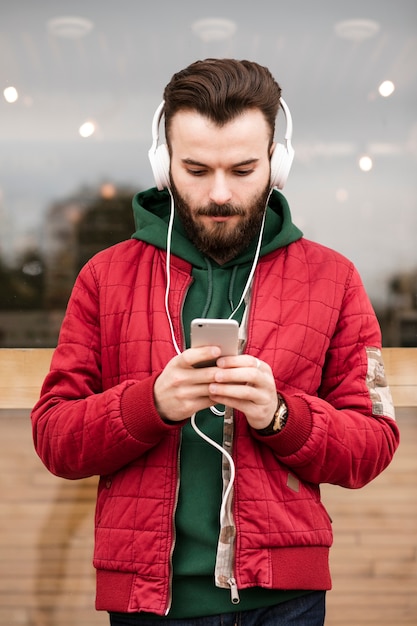 Kostenloses Foto mittlerer schusskerl mit den kopfhörern, die smartphone betrachten