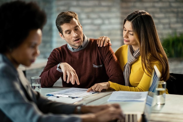 Kostenloses Foto mittleres erwachsenes paar, das hypothekenvertrag analysiert, während es sich auf einem treffen mit einem immobilienmakler befindet der fokus liegt auf einer frau, die auf ein dokument zeigt