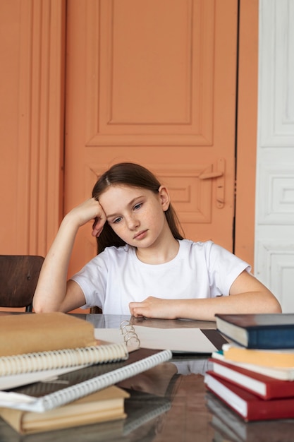 Mittleres Schuss gelangweiltes Mädchen, das mit Büchern am Schreibtisch sitzt