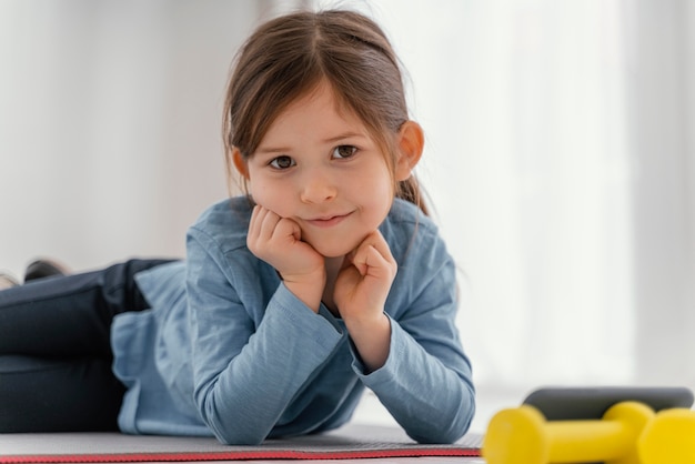 Kostenloses Foto mittleres schussmädchen, das auf matte sitzt