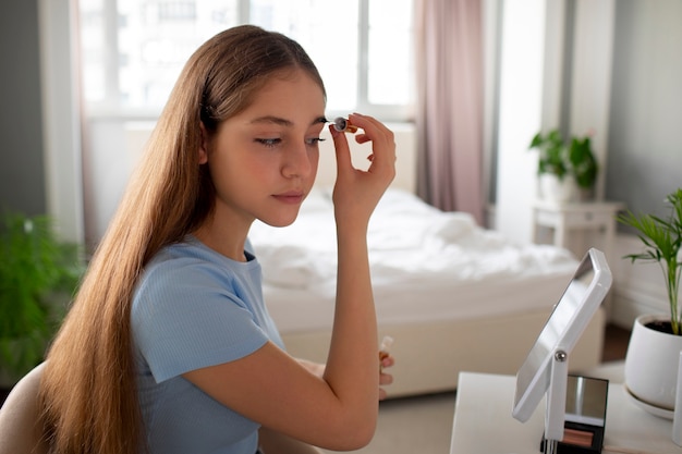 Kostenloses Foto mittleres schussmädchen, das make-up aufsetzt