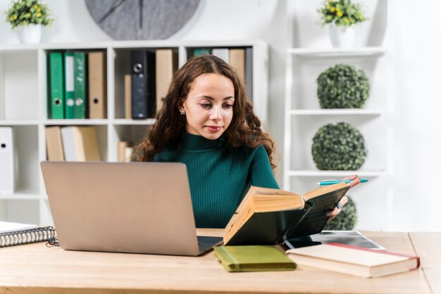 Mittleres Schusssmileymädchen, das mit Wörterbuch und Laptop studiert