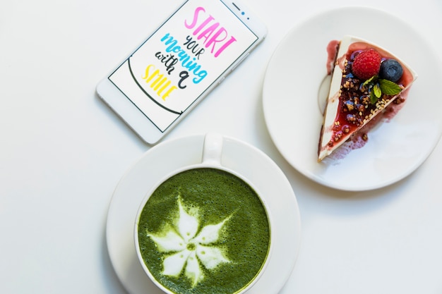 Kostenloses Foto mobiler bildschirm mit meldung auf dem bildschirm; matcha grüner tee tasse und kuchen slice auf platte auf weißem hintergrund