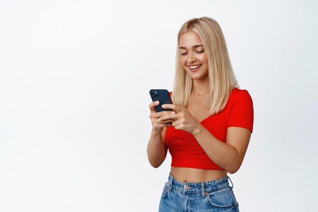 Mobilfunktechnologie Junge, blonde Frau, die mit dem Handy telefoniert und lächelnd Nachrichten sendet oder eine Bestellung auf dem weißen Hintergrund des Smartphones platziert