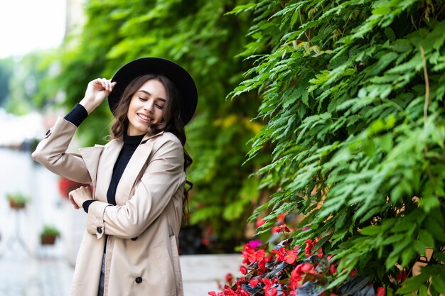 Mode-Außenfoto der jungen hübschen Frau im eleganten Outfit und im schwarzen Hut, die auf der Straße gehen