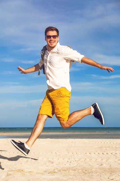 Mode-Außenporträt des gutaussehenden Mannes im hellen trendigen lässigen Outfit, das am tropischen Strand geht