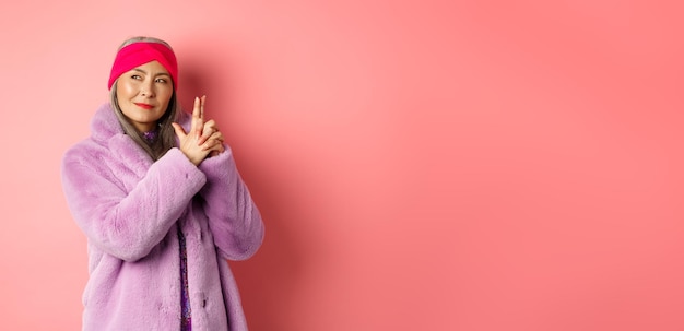 Mode- und Einkaufskonzept Coole und stilvolle asiatische Seniorin in lila Kunstpelzmantel, die Finger macht