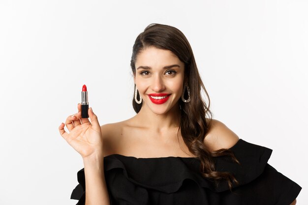 Mode- und Schönheitskonzept. Schöne Frau im schwarzen Kleid, das roten Lippenstift zeigt und lächelt, stehend auf weißem Hintergrund. Platz kopieren