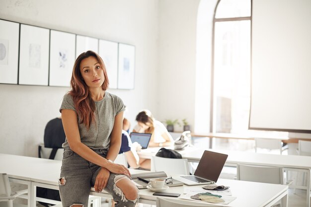 Modedesign-Lehrling, der in einem Coworking Space oder auf einem Campus studiert, der auf Tisch mit Laptop- und Textilproben sitzt Trendy Berufskonzept.