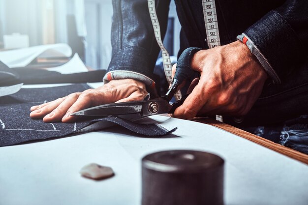 Modedesigner schneidet Stoff mit einer Schere ab. Er trägt Jeans. Fotoshooting in Nahaufnahme.
