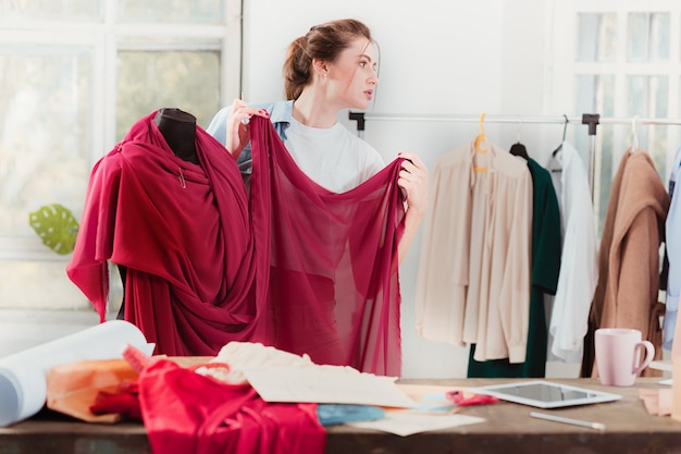 Modedesignerin, die im Studio arbeitet, sitzt auf dem Schreibtisch