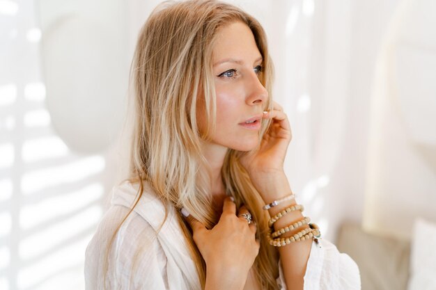 Modefoto einer schönen blonden Frau in weißer Sommerkleidung, die während der Ferien in einem modernen Hotel posiert