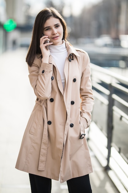 Modefrau, die auf dem Handy in einer Stadtstraße geht und spricht