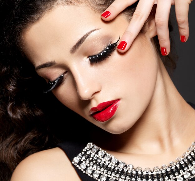 Modefrau mit modernem kreativem Make-up unter Verwendung der roten Maniküre der falschen Wimpern