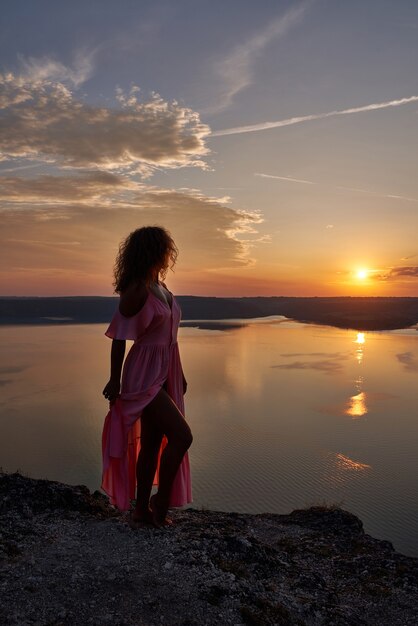 Model posiert im Kleid auf dem Hintergrund des Sonnenuntergangs in der Nähe des Sees