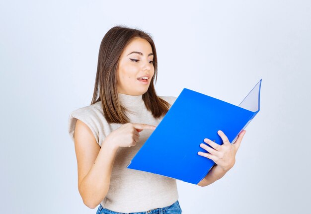 Modell der jungen Frau, das einen blauen Ordner über weiße Wand betrachtet.