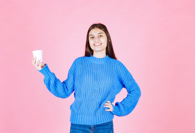 Modell des jungen Mädchens, das einen Plastikbecher auf rosa Wand hält.