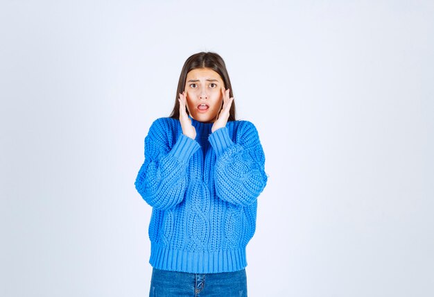 Modell des jungen Mädchens im blauen Pullover, der den Mund mit einer Hand auf Weißgrau konischt.