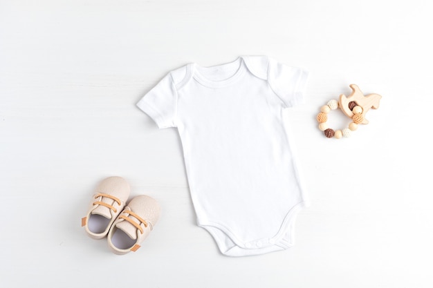 Modell eines weißen babybodys aus bio-baumwolle mit umweltfreundlichem babyzubehör. onesie-vorlage für marke, logo, werbung. flache lage, ansicht von oben