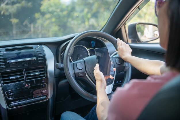 Modellbild einer Frau, die ein Mobiltelefon mit leerem Bildschirm hält und benutzt, während sie ein Auto fährt, für GPS, Lifestyle-Foto im Auto, Innenraum, Vorderansicht. Mit der Frauenhand, die Telefon hält.
