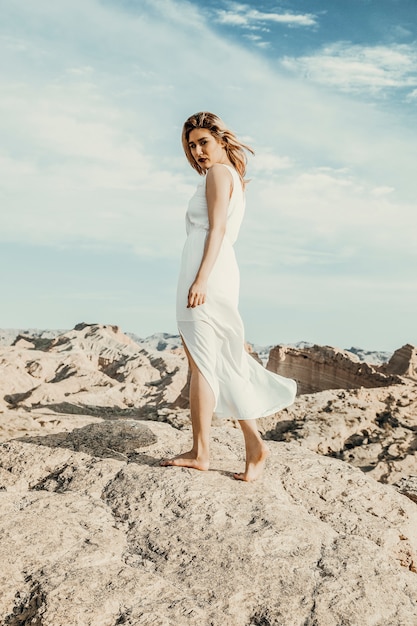 Modemodell im weißen Kleid, das auf den Wüstensteinen geht