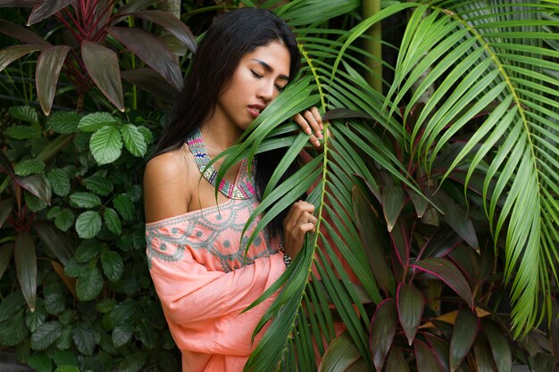 Modeporträt der attraktiven asiatischen Frau, die im tropischen Garten aufwirft. Trägt Boho-Kleid und stilvolle Accessoires.