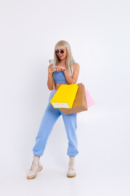 Modeporträt der jungen blonden Frau mit langen herrlichen geraden Haaren halten bunte Einkaufstaschen