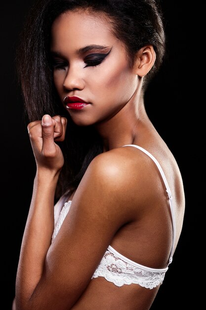 Modeporträt des schönen amerikanischen schwarzen weiblichen Brunettemädchenmodells mit den hellen Make-uproten Lippen in der weißen Wäsche. Saubere Haut. Schwarzer Hintergrund