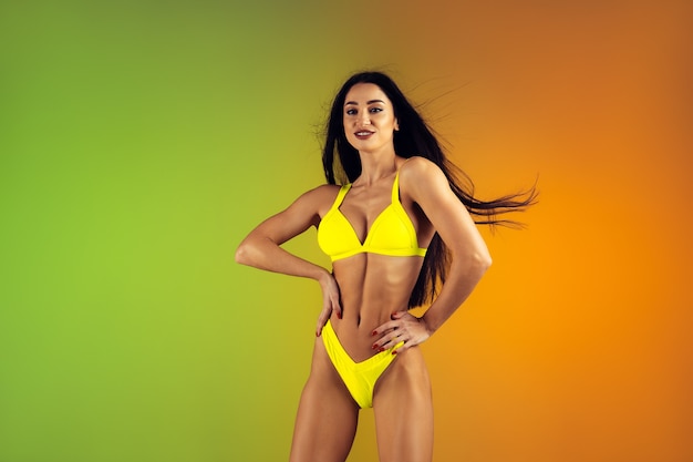 Modeporträt einer jungen, fitten und sportlichen frau in stilvoller gelber luxusbadebekleidung an einer wand mit farbverlauf, perfekter körper, der für den sommer bereit ist