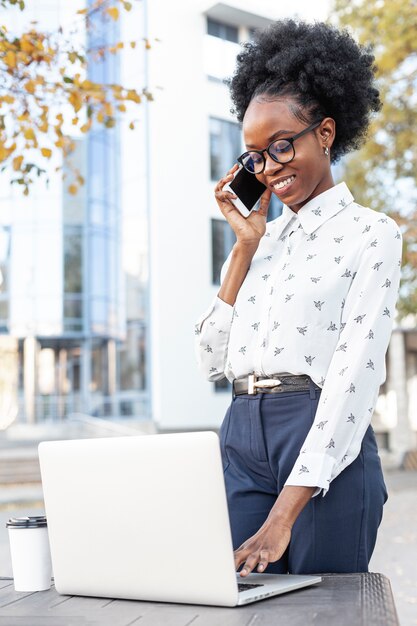 Moderne Frau, die an Laptop arbeitet und über Telefon spricht