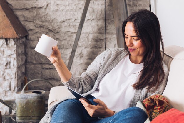 Moderne Frau, die auf dem Sofa unter Verwendung einer Tablette sitzt